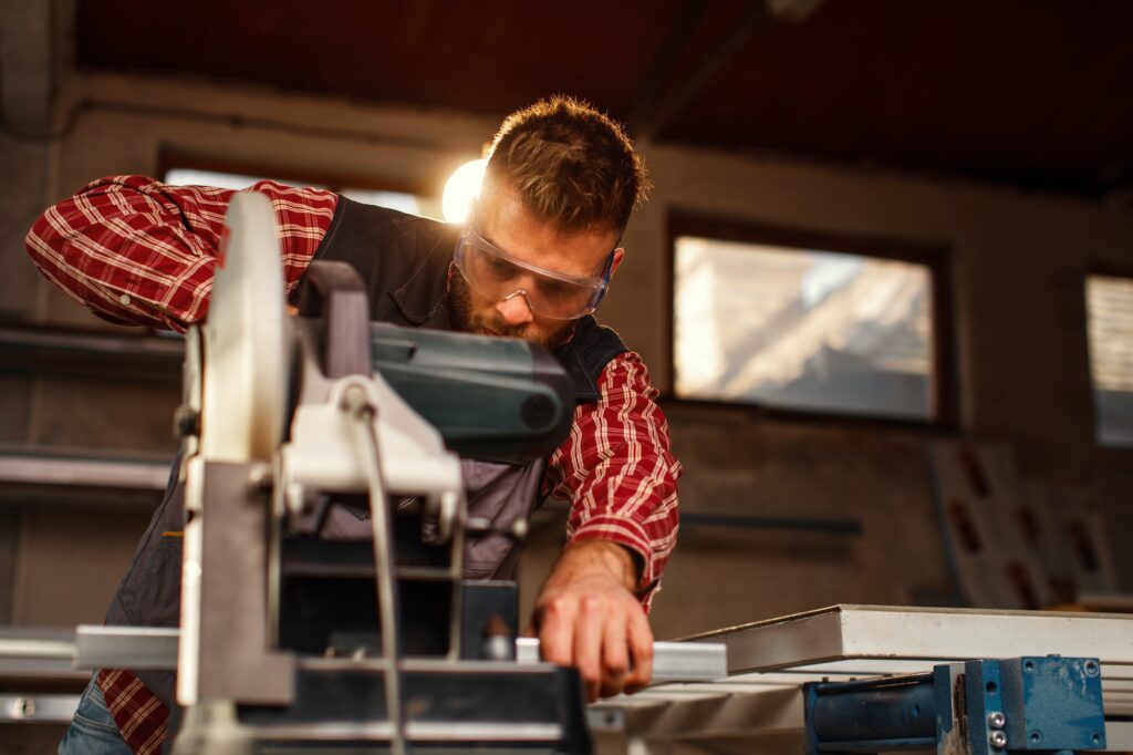 Young man work in home workshop garage with a grinder cuts metal bar